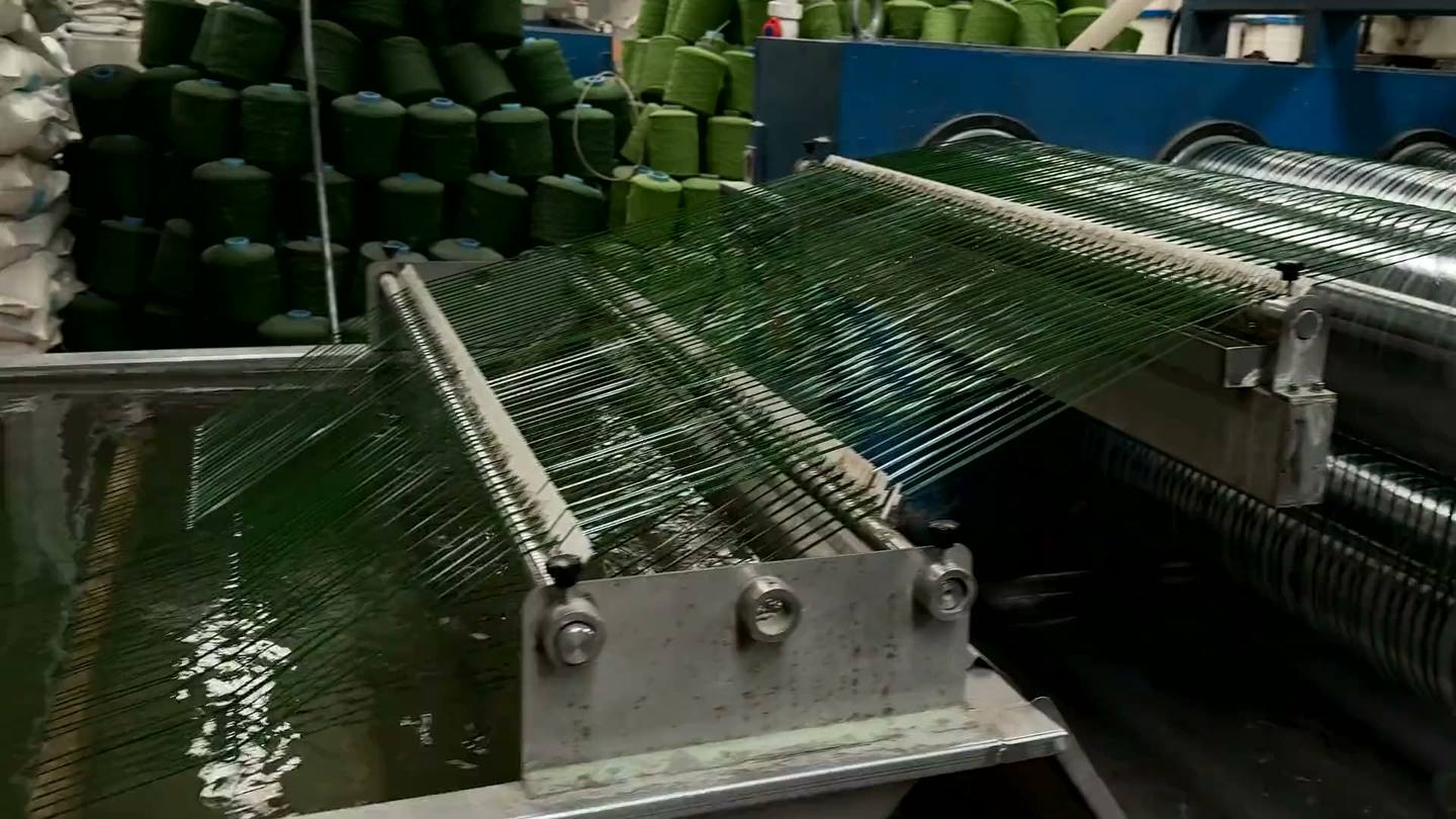 Artificial turf running over the rollers of a tufting line
